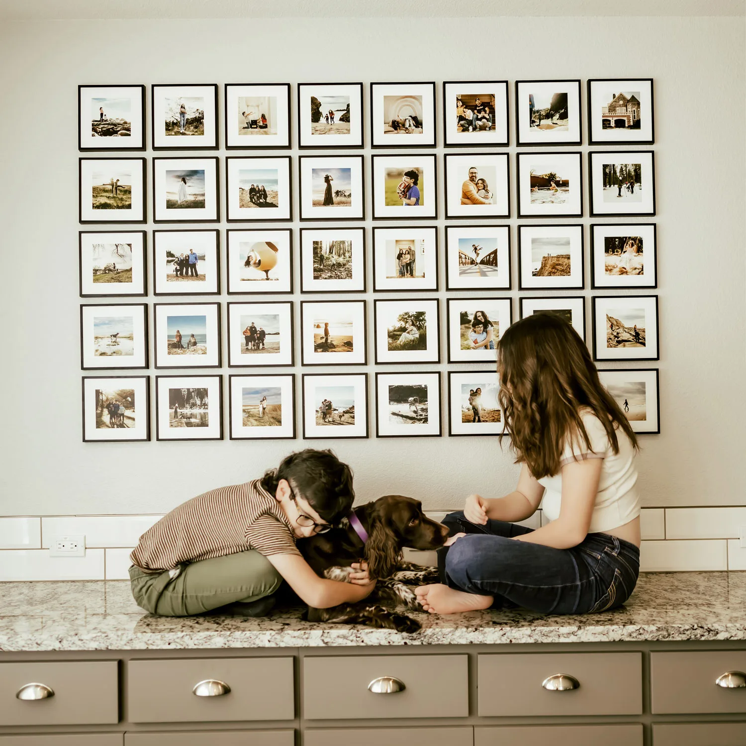 A large grid of black Mixtiles frames above a family and their dogs